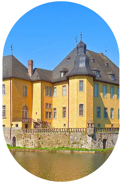 Ein altes Schloss mi gelben Mauern steht an einem Gewässer